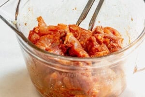 tossing cubed chicken thighs with olive oil and spices in a bowl.