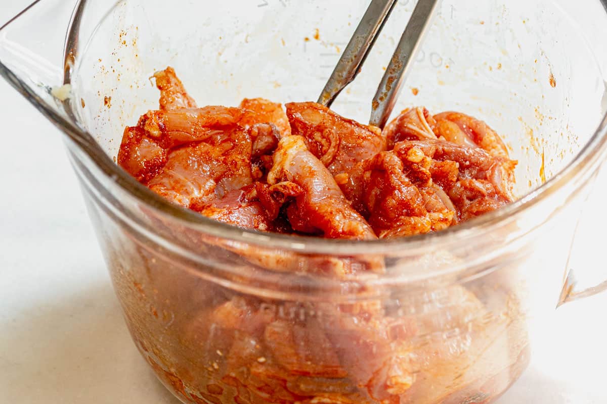 tossing cubed chicken thighs with olive oil and spices in a bowl.