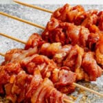 Seasoned and cubed chicken threaded on wooden skewers on a cutting board.