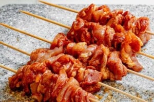 Seasoned and cubed chicken threaded on wooden skewers on a cutting board.