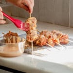 Brushing bang bang sauce onto chicken skewers.