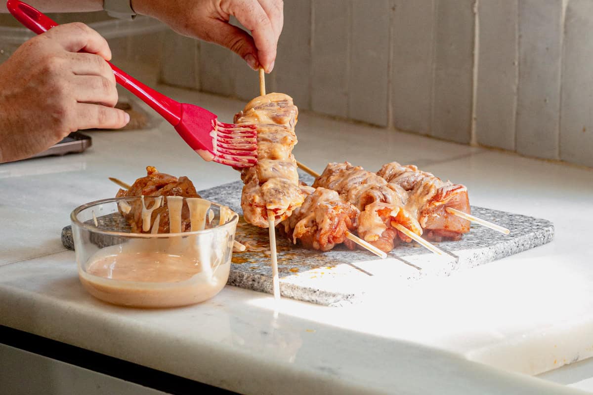 Brushing bang bang sauce onto chicken skewers.