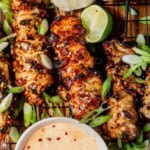 a tray of bang bang chicken skewers with lime and green onions to garnish.