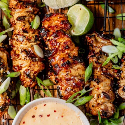 a tray of bang bang chicken skewers with lime and green onions to garnish.