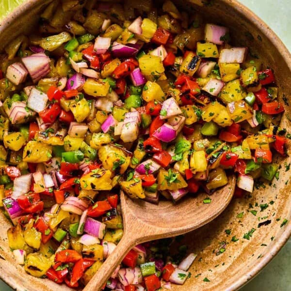 a wooden bowl of grilled pineapple salsa with a wood serving spoon.