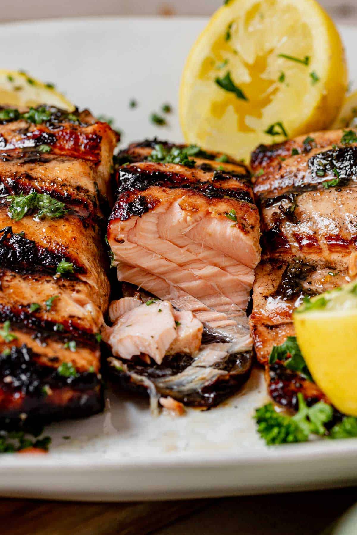 Close-up of perfectly grilled salmon fillet with char marks, flaky interior, and fresh parsley, served with lemon wedges.