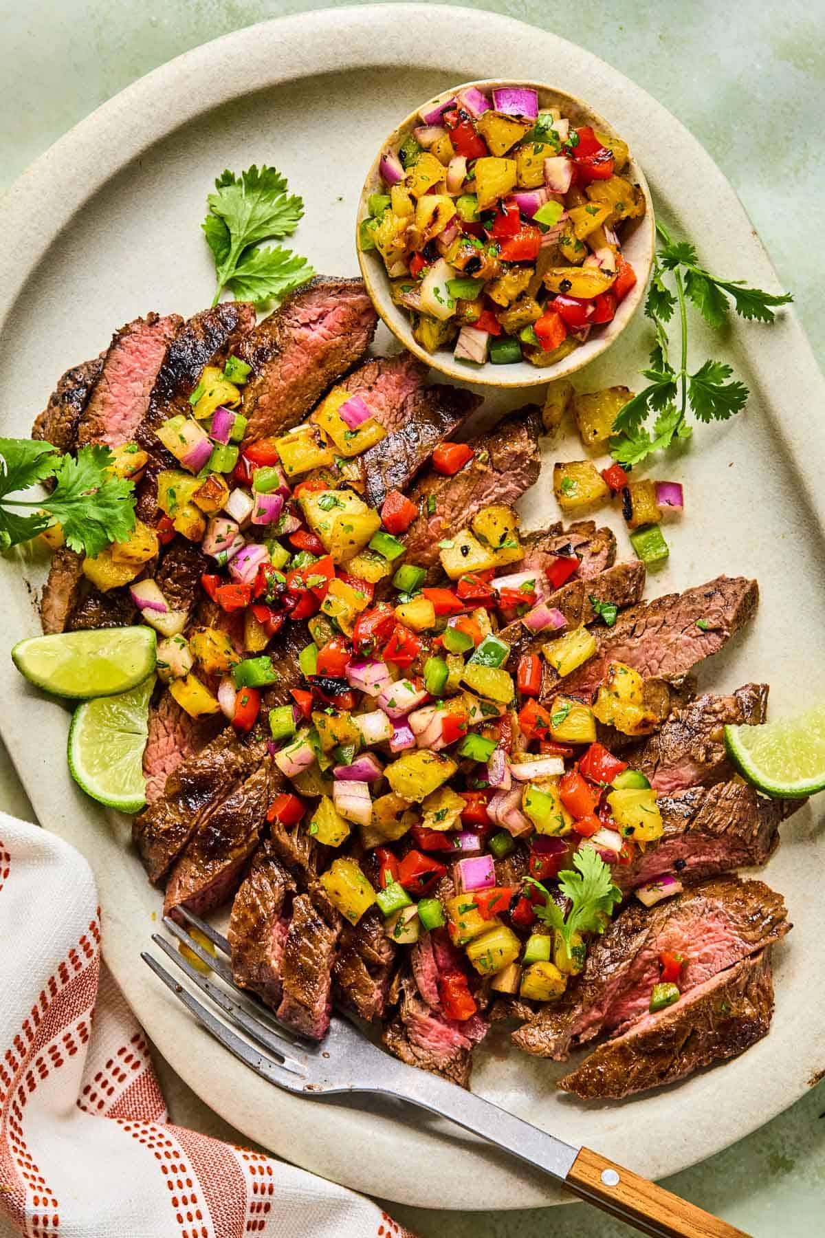 grilled flank steak sliced on a large plate with pineapple salsa