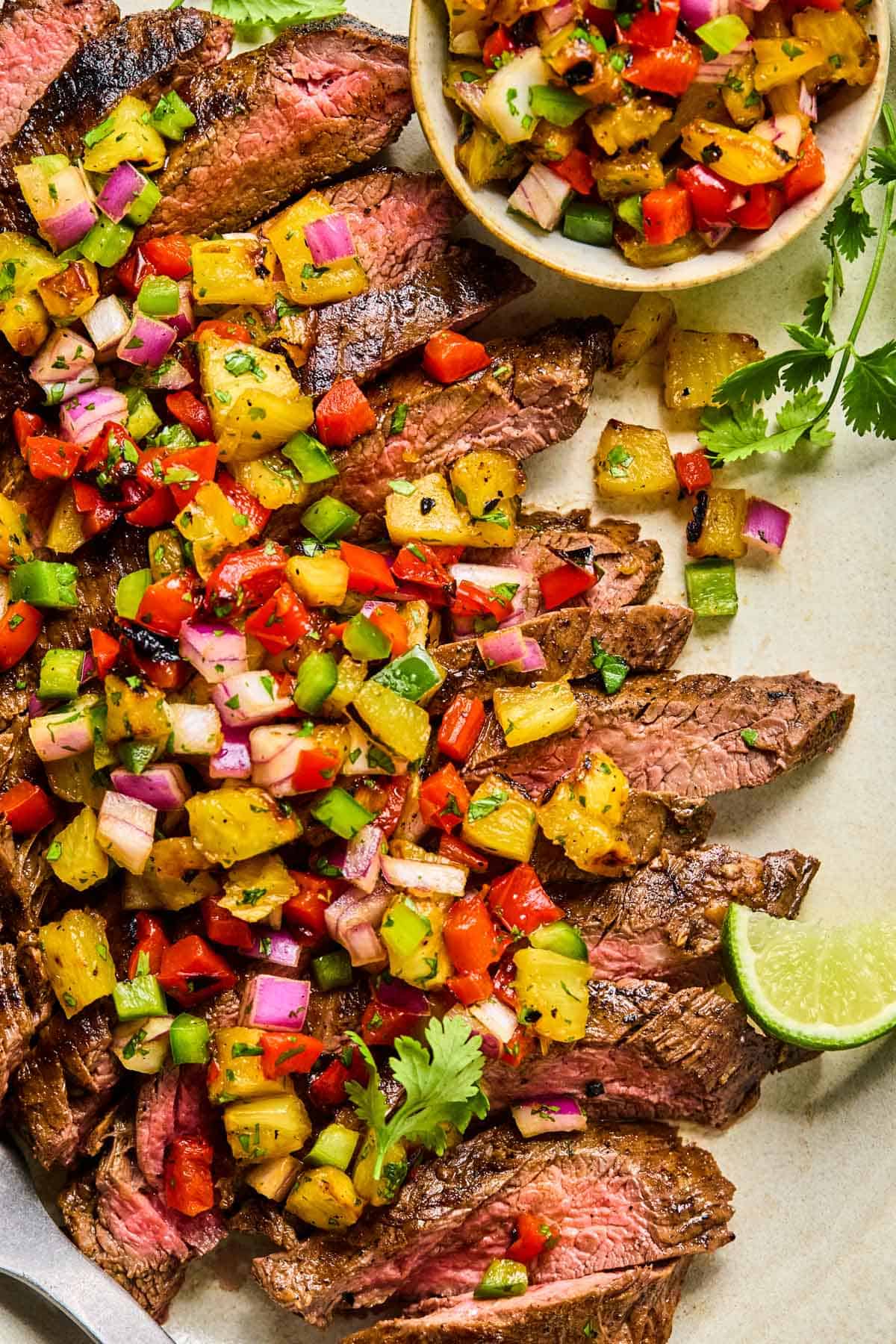 grilled flank steak thinly sliced on a plate with grilled pineapple salsa on top.