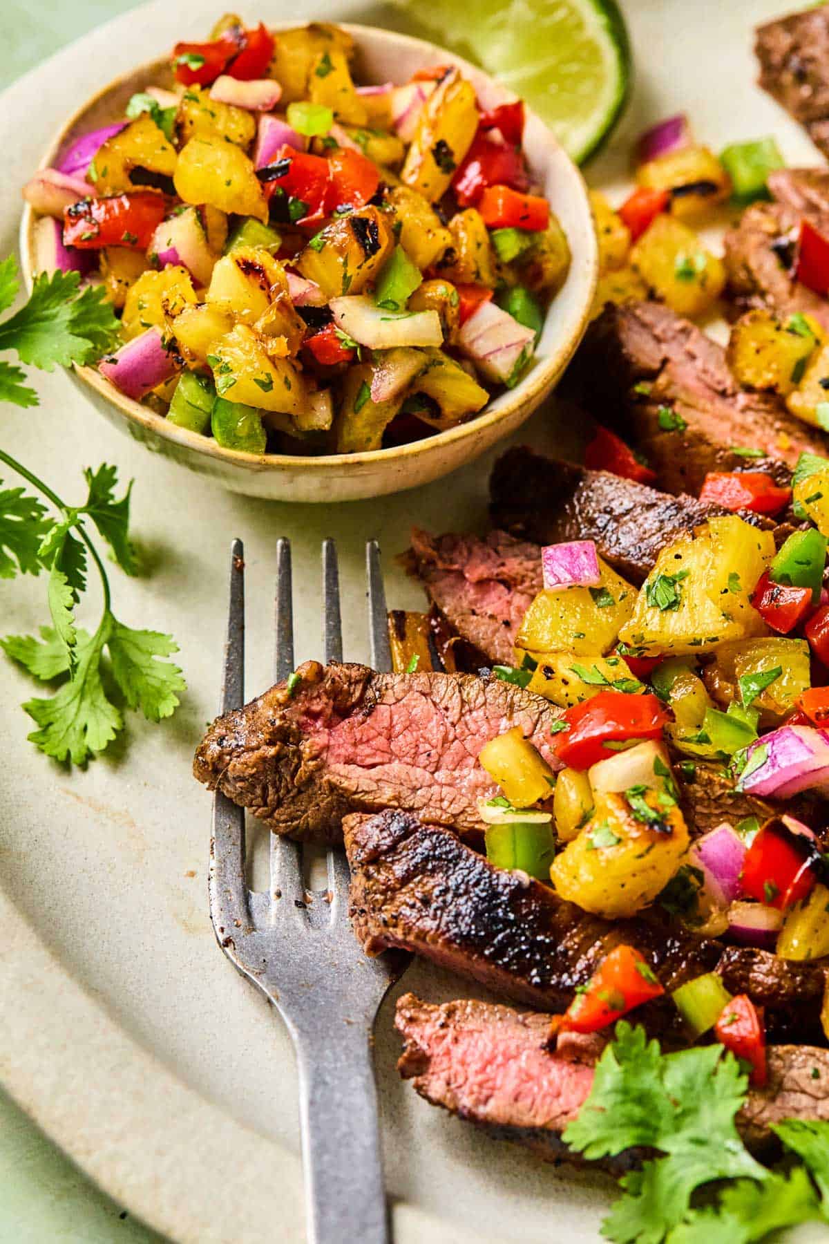 fork on a plate with grilled flank steak and pineapple salsa