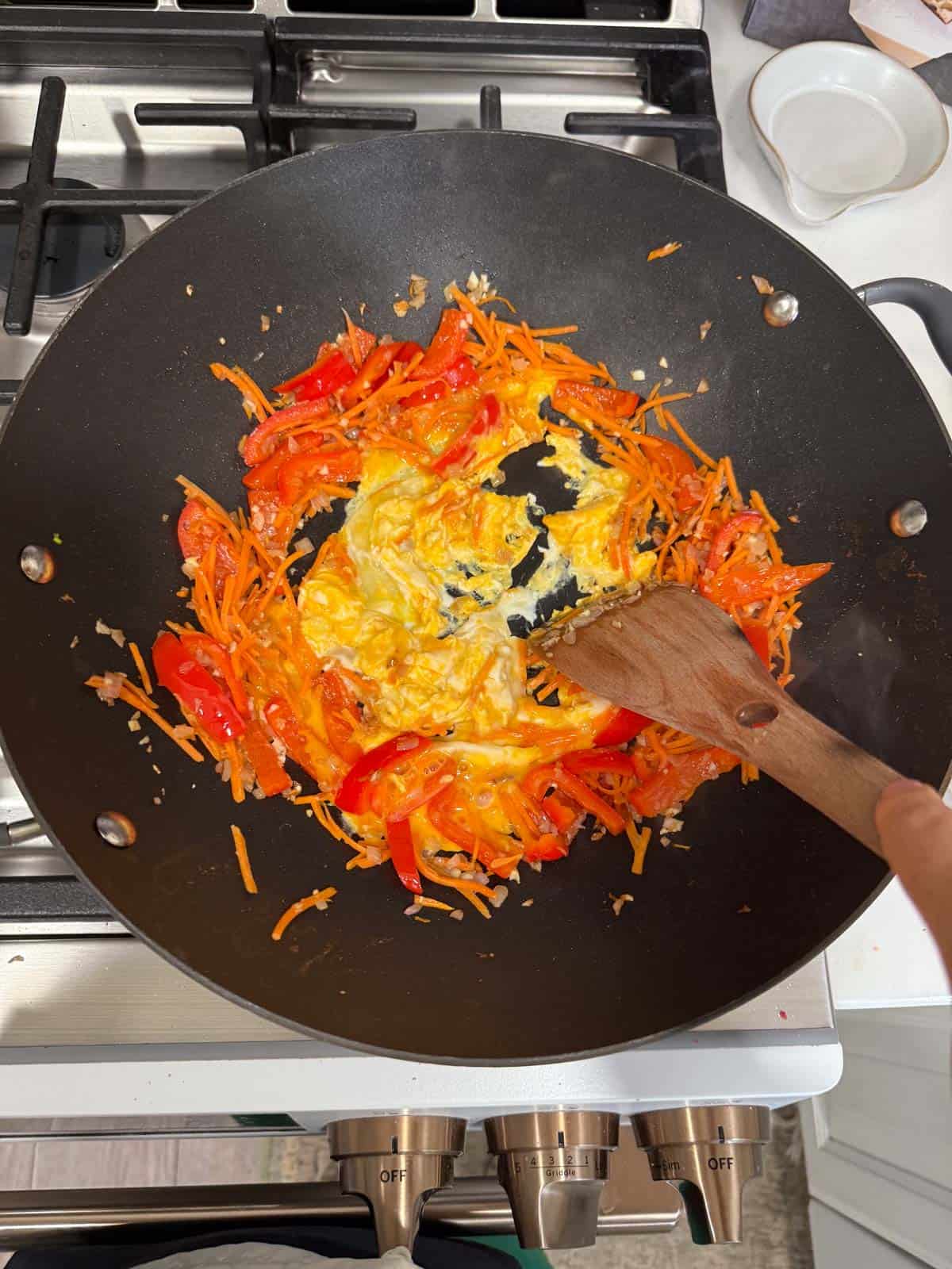 scrambling eggs in a wok with pad thai vegetables.