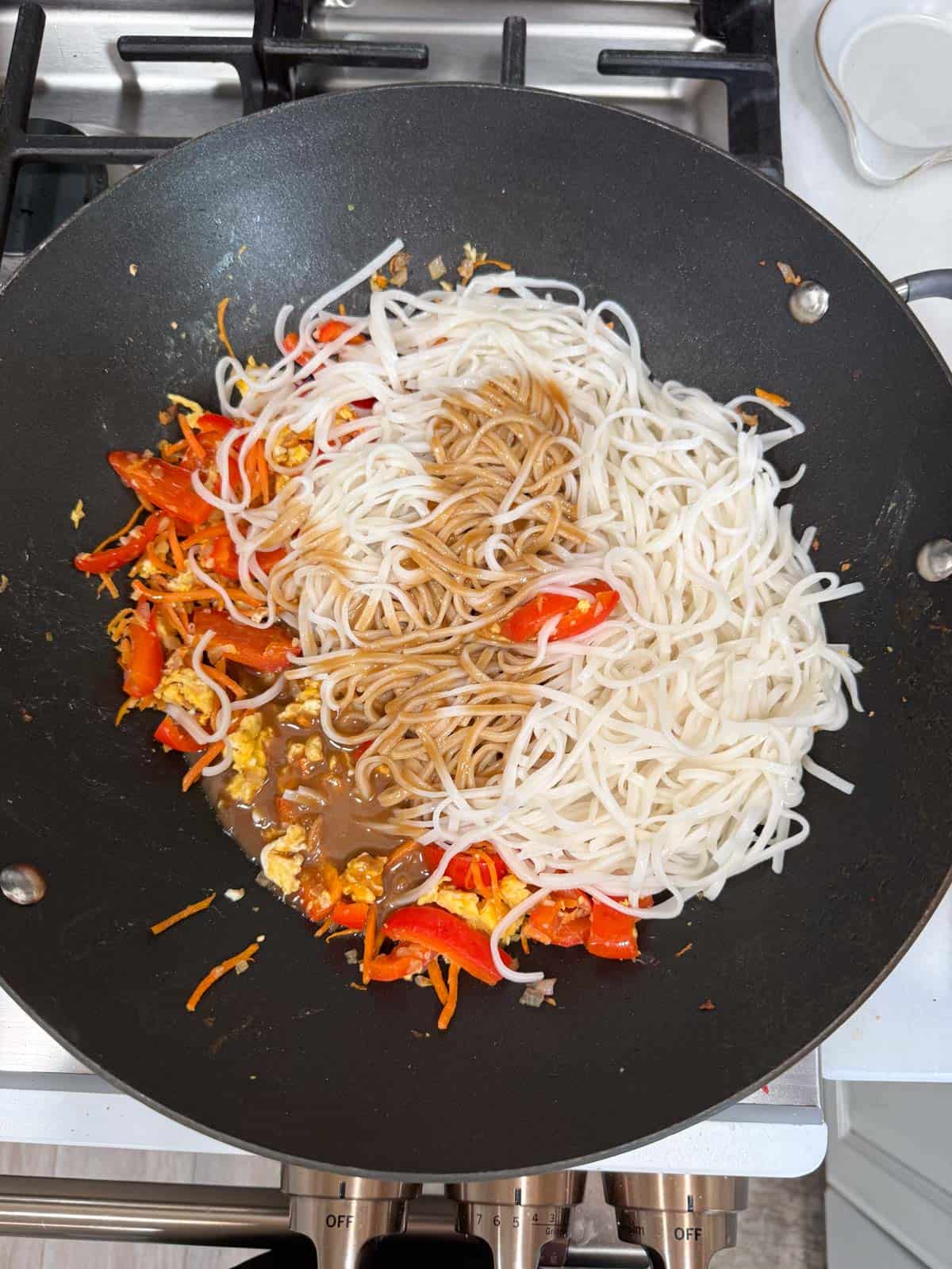 pad thai sauce and cooked noodles in a wok with pad thai vegetables.