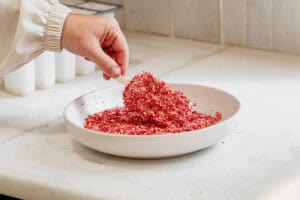 coating a strawberry ice cream bar in a cookie strawbery coating in a plate.