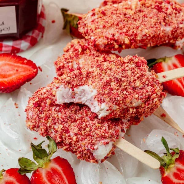 Three strawberry shortcake ice cream bars stacked on a tray of ice with a bite missing from the top one.