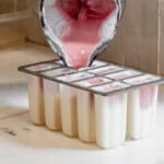 pouring strawberry filling for ice cream bars on top of the vanilla layer in popsicle molds.