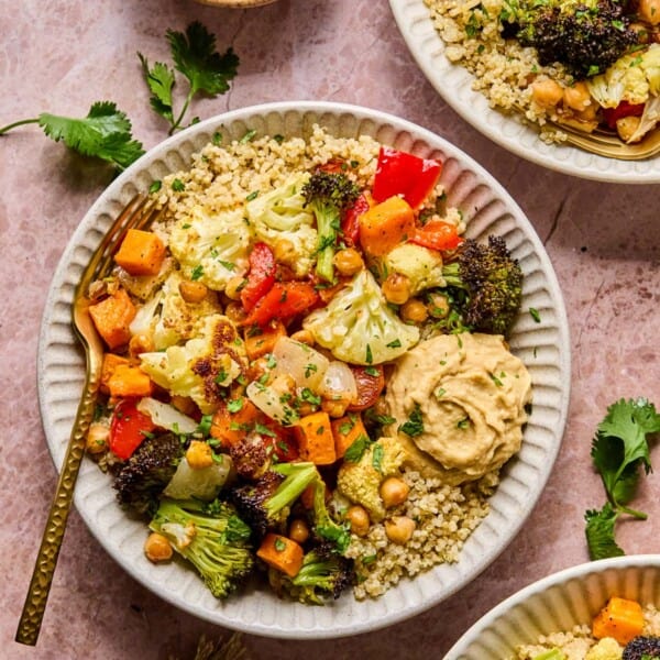 roasted veggie quinoa bowl ingredients in a white bowl on the table with a fork in it