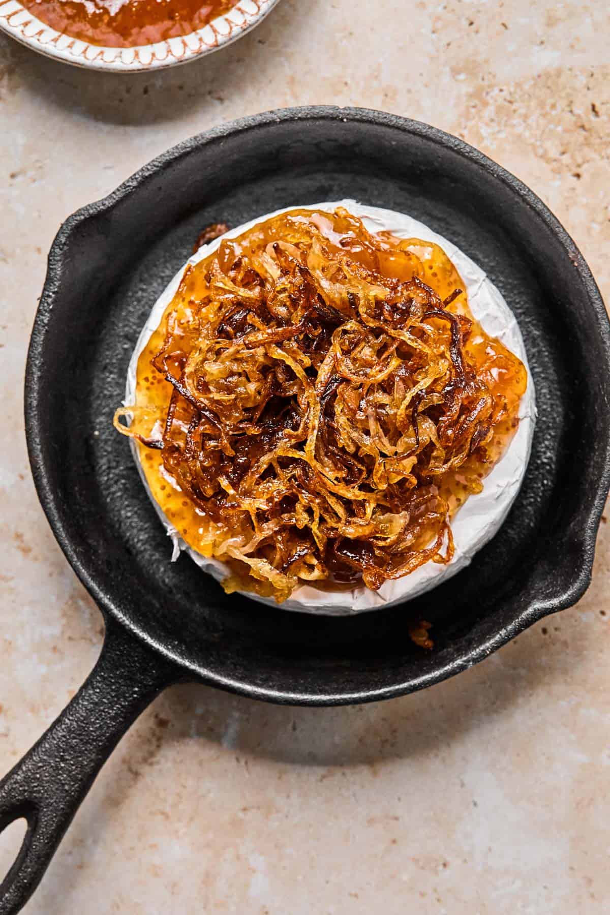 wheel of brie with fig jam and caramelized onions on top sitting in a cast iron pan