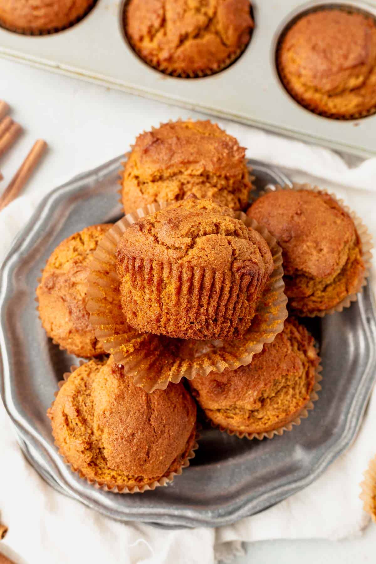 These gluten free pumpkin muffins are filled with pure pumpkin, fall spices and chocolate chips. Enjoy a delicious muffin in the morning this fall without all the gluten! gluten free pumpkin muffins piled on a plate. top muffin has the cupcake wrapper unwrapped