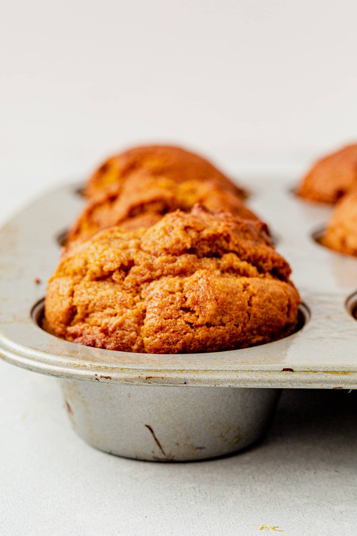 up close of the side view of a gluten free pumpkin muffin cooling in a muffin tin