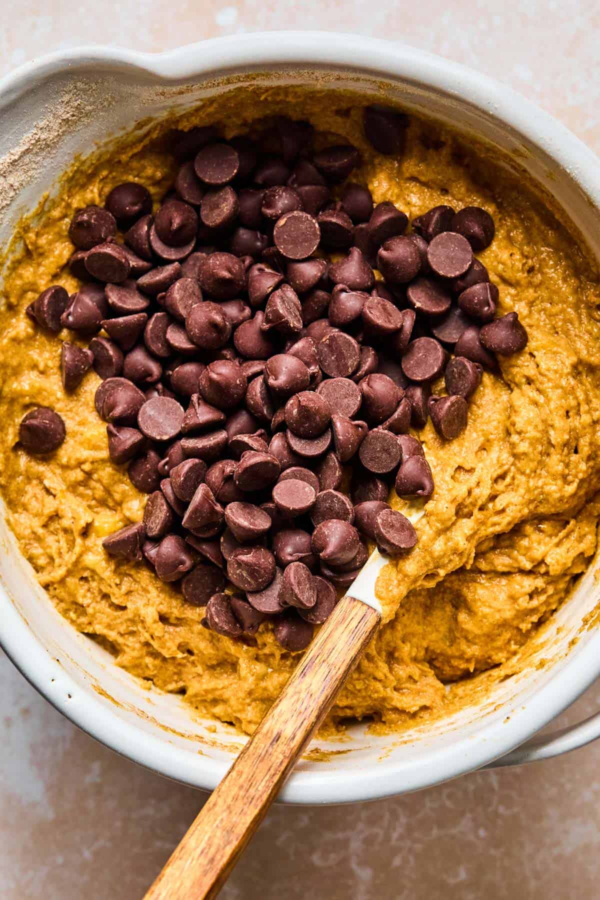 dark chocolate chips added to banana pumpkin bread mix in a mixing bowl with a spatula