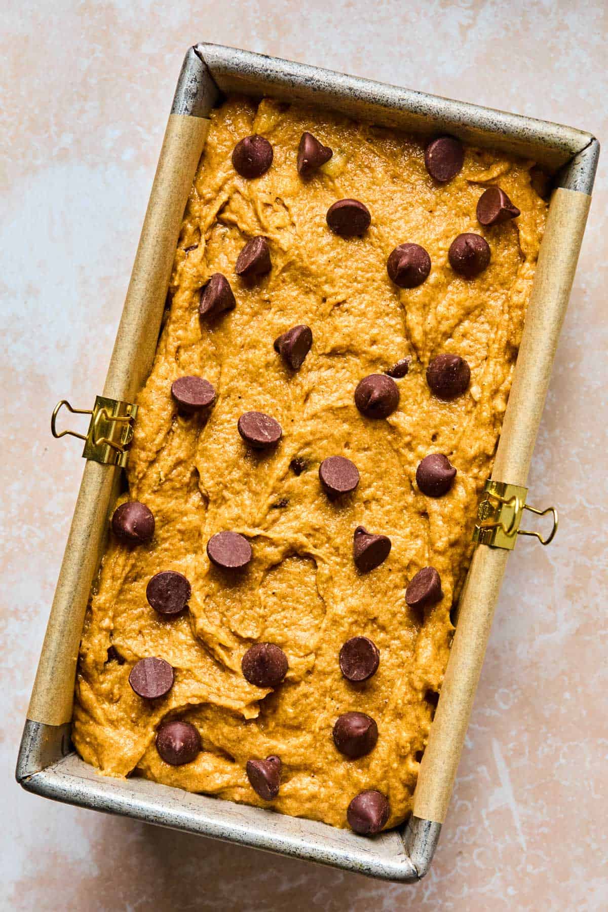 healthy banana pumpkin bread batter added to a bread loaf pan with parchment paper clipped to the sides of the pan