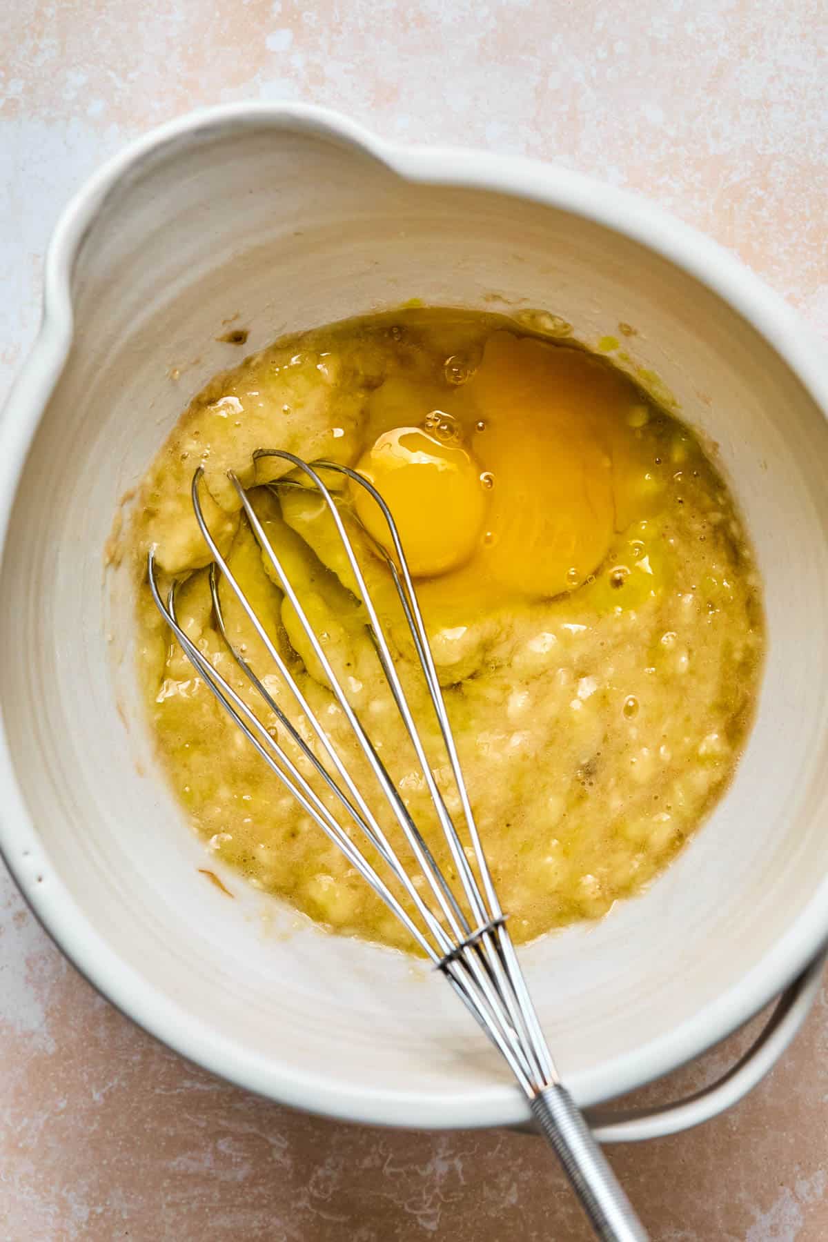 wet ingredients added to mashed banana in a mixing bowl with a whisk