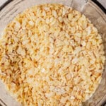 Close-up of a glass mixing bowl filled with a combination of rolled oats and puffed rice cereal on a neutral kitchen counter.