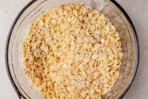 Close-up of a glass mixing bowl filled with a combination of rolled oats and puffed rice cereal on a neutral kitchen counter.