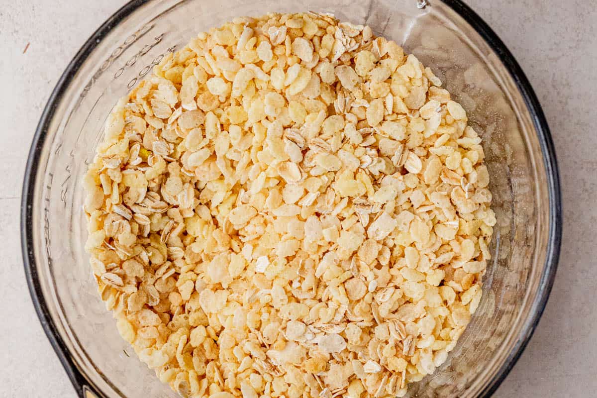Close-up of a glass mixing bowl filled with a combination of rolled oats and puffed rice cereal on a neutral kitchen counter.