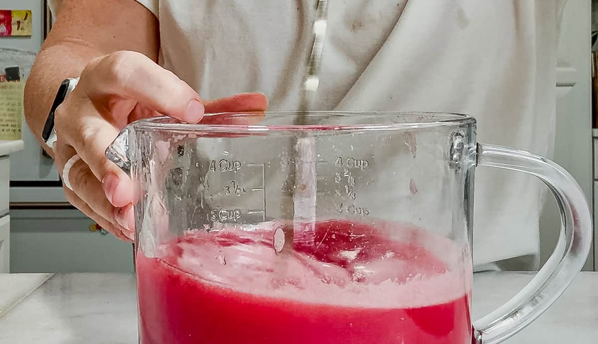 mixing a watermelon vodka cocktail in a glass pitcher with a cocktail spoon.