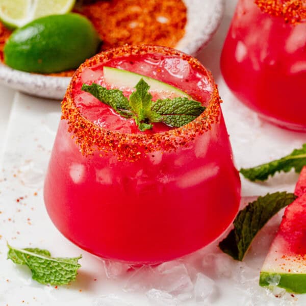 Close-up of a watermelon vodka cocktail in a glass rimmed with Tajin, garnished with mint and watermelon.
