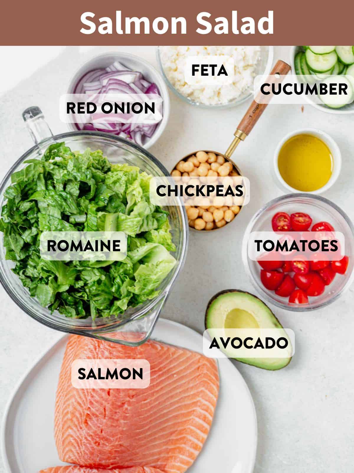 Raw salmon fillets with romaine, cucumber, tomatoes, avocado, chickpeas, feta, and onion prepared for salad.
