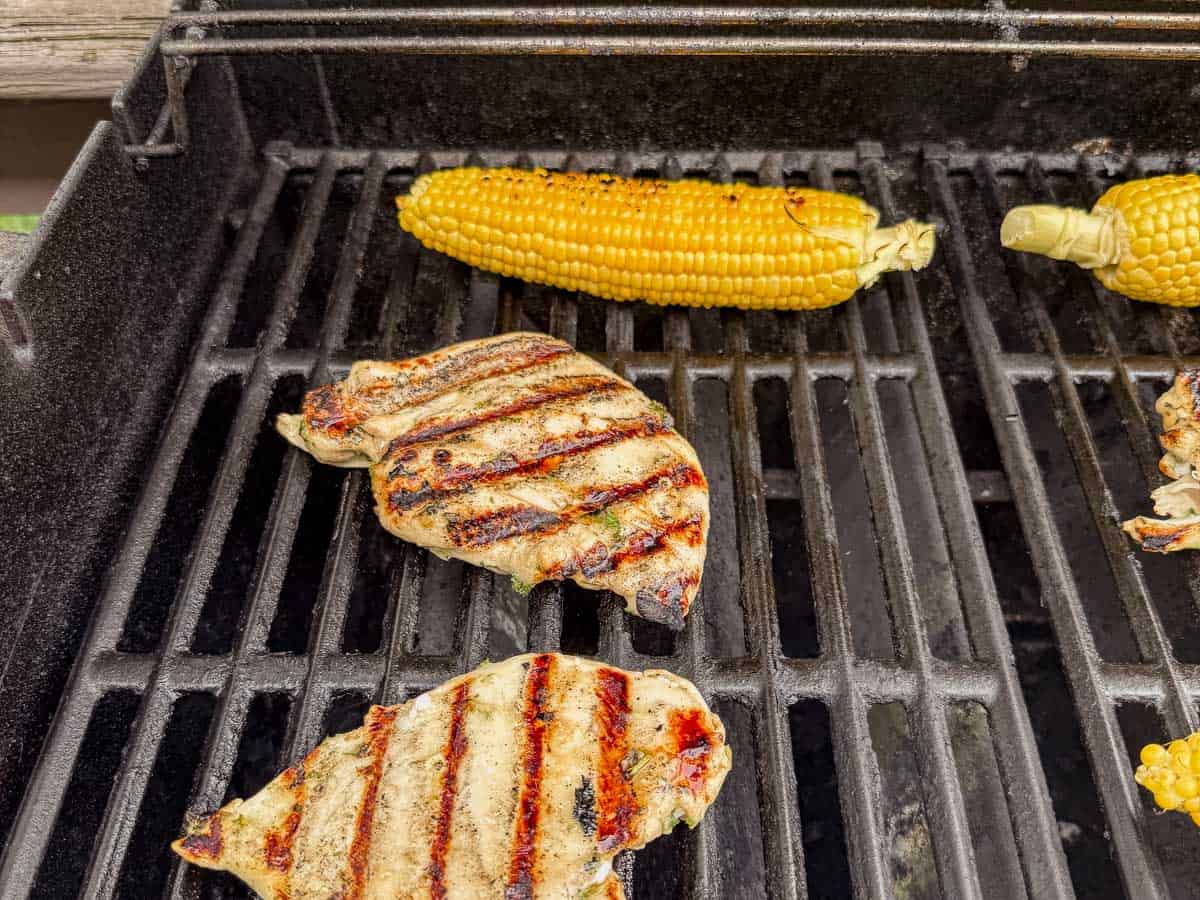Chicken breasts and corn on the cob grilling over open grates with visible char marks.