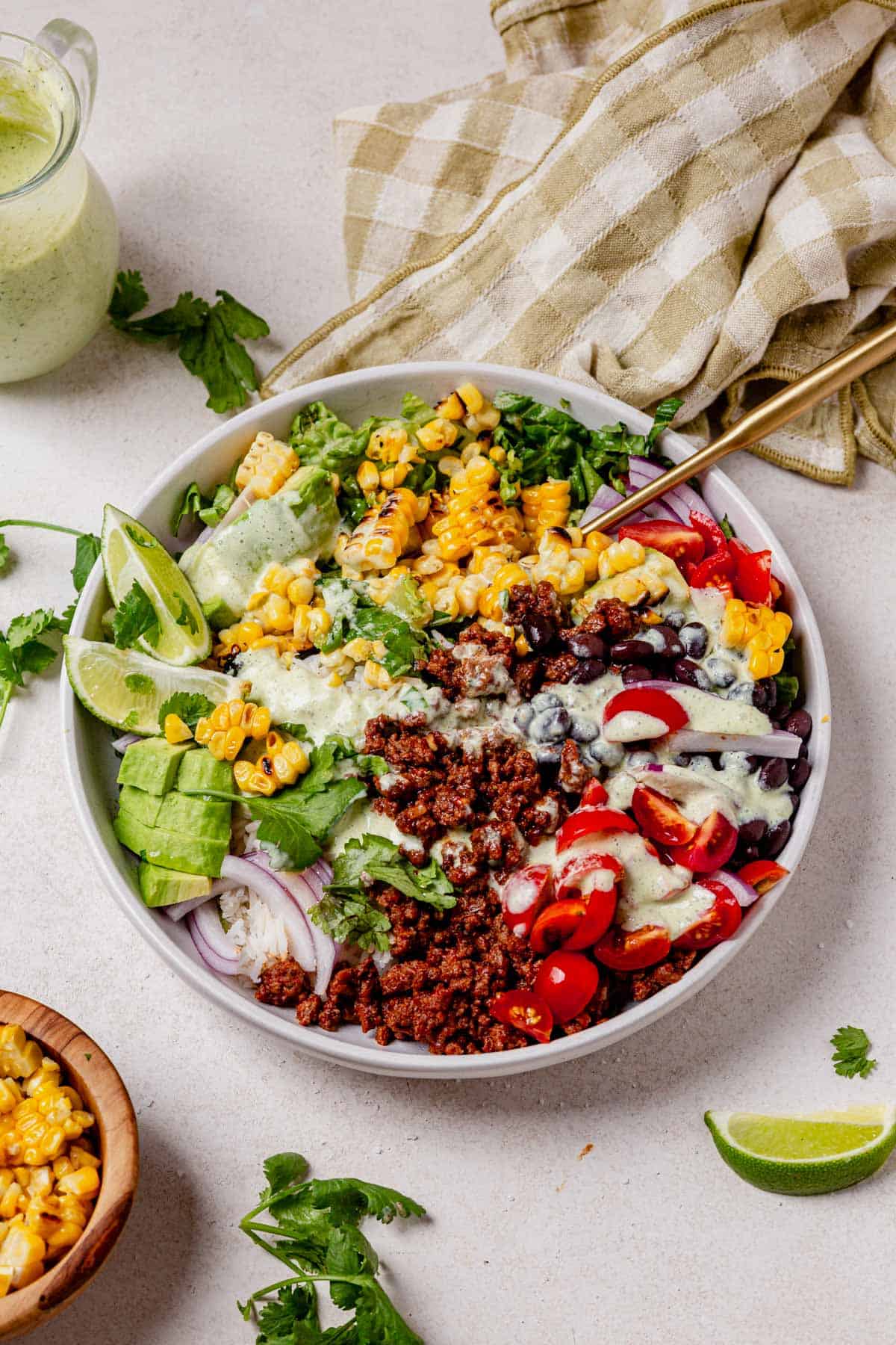 A ground beef taco bowl topped with tomatoes, corn, black beans, avocado, and cilantro.