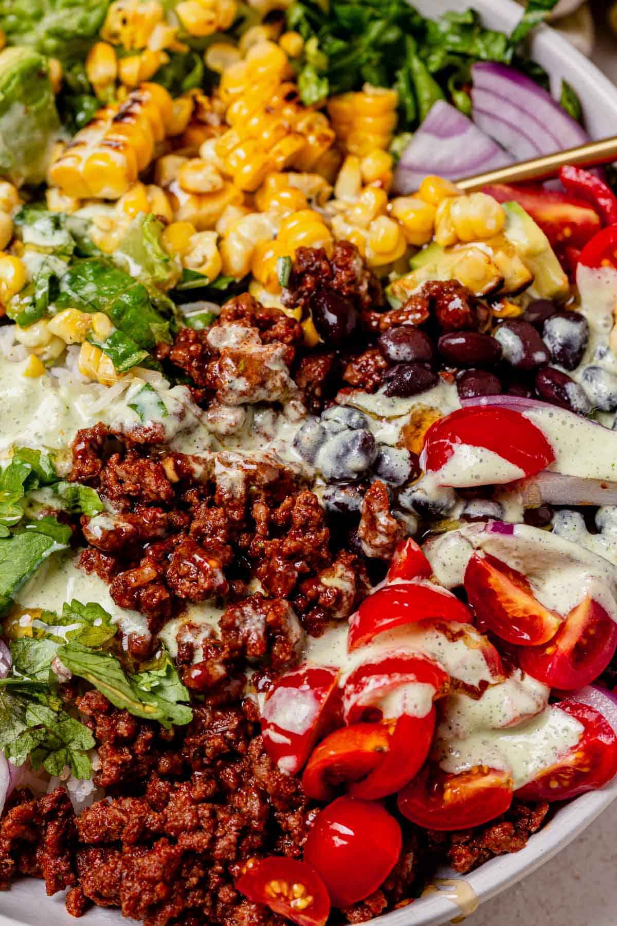 ground beef, rice, lettuce, tomatoes, and corn in a taco bowl drizzled with creamy dressing.