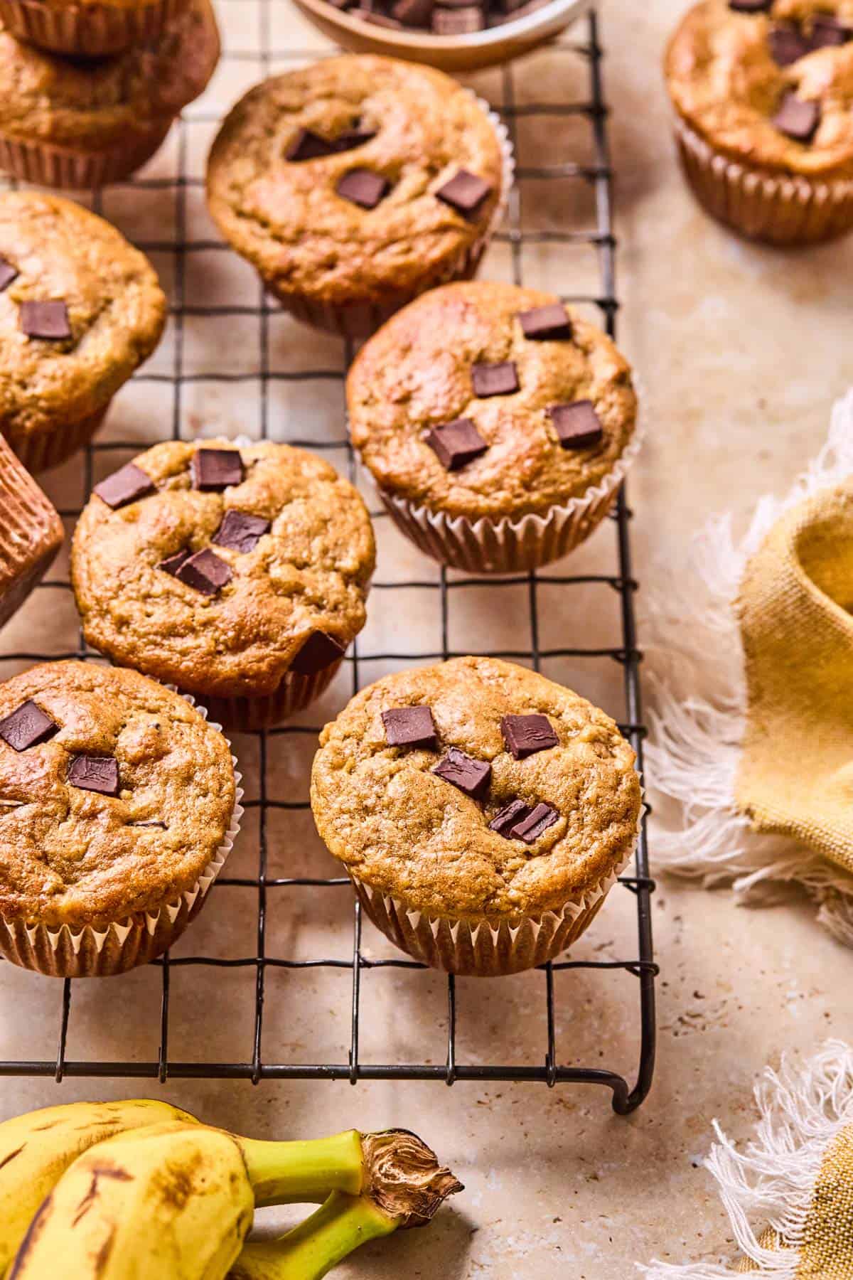 chocolate chip almond flour banana muffins cooling in white wrappers on a black cooling rack.