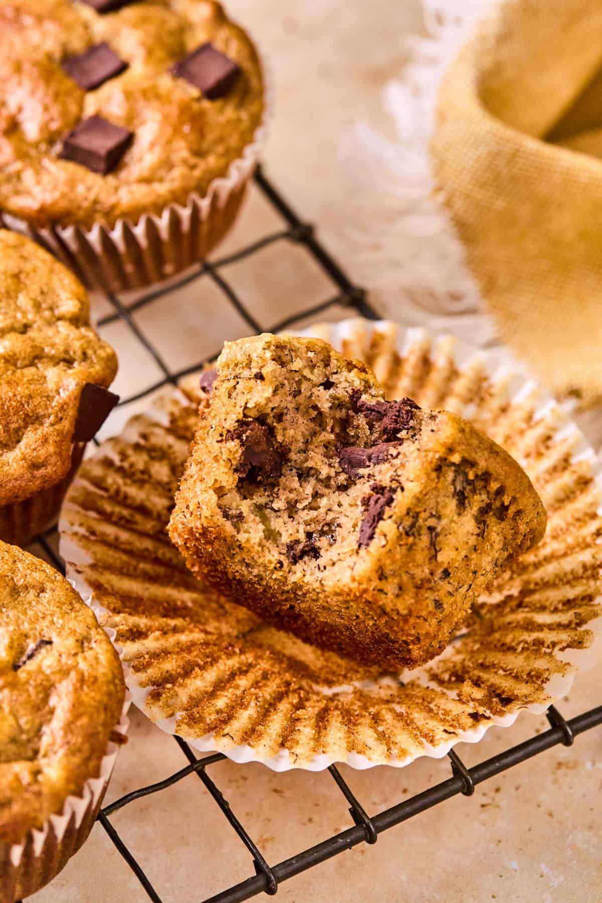 healthy almond flour banana muffin with a bite taken out of it, resting on an open cupcake wrapper on a cooling rack.