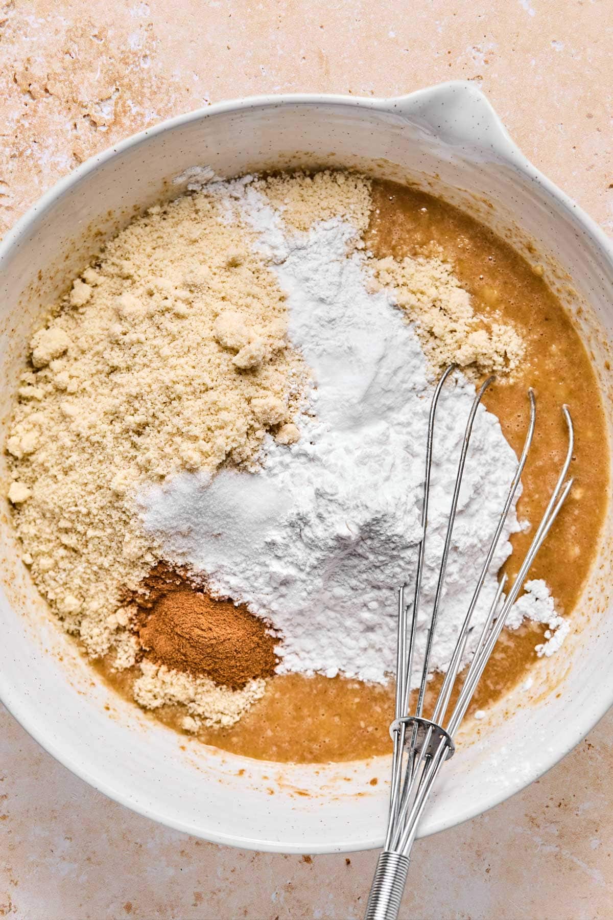 dry ingredients for healthy banana muffins added to combined wet ingredients with a whisk sitting in the bowl.
