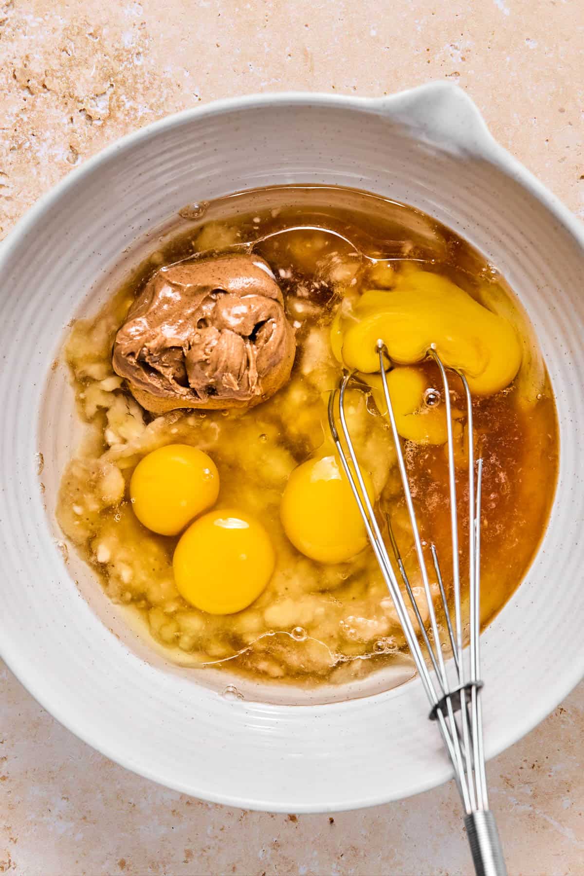wet ingredients for healthy banana muffins in a bowl with a whisk.