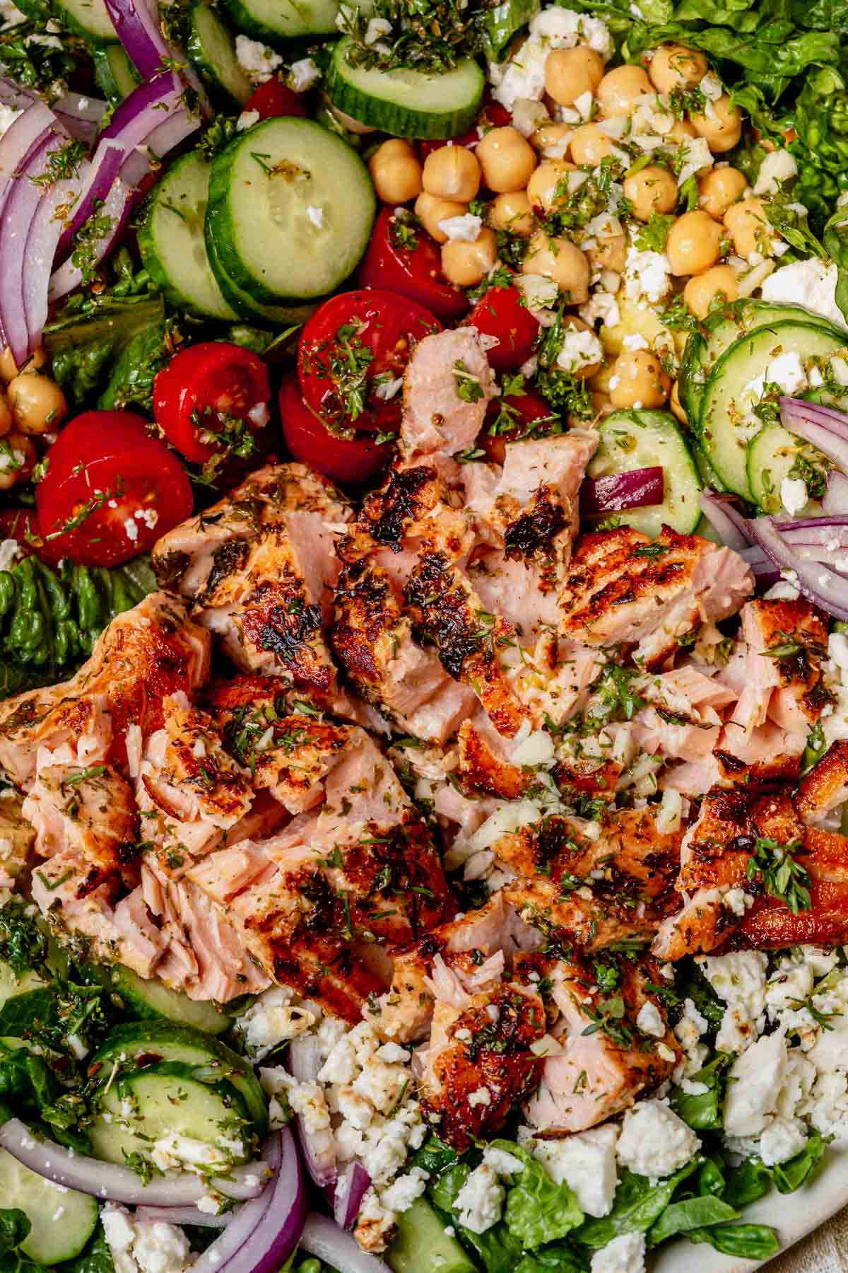 Close-up of flaked cooked salmon on salad with cucumbers, tomatoes, feta, and onion.