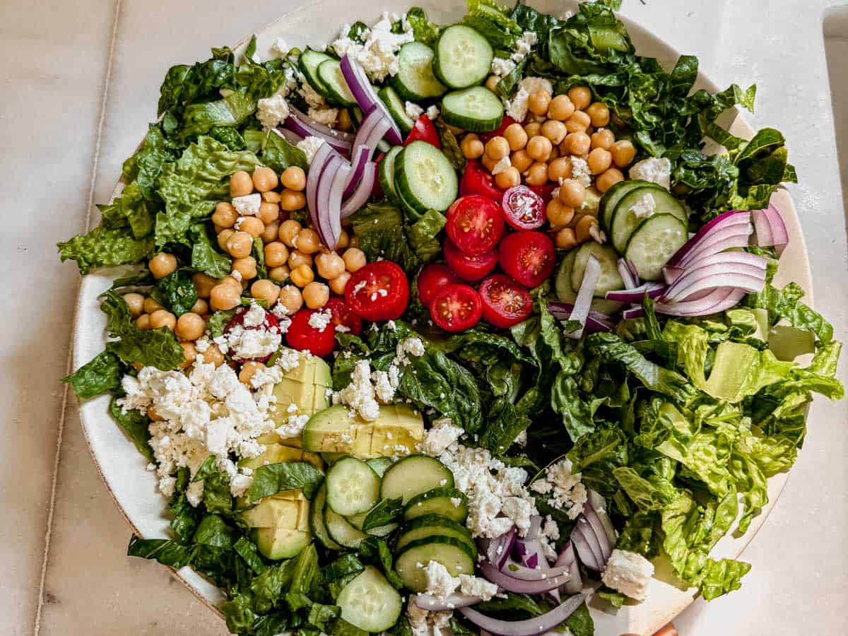 Salad ingredients including romaine, cucumbers, tomatoes, chickpeas, and feta in a serving bowl.