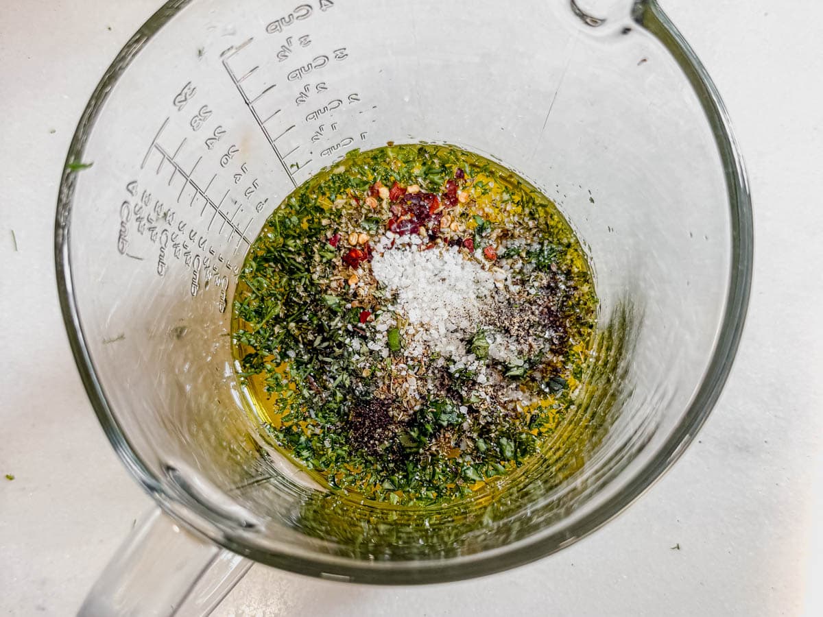 Mixing bowl with salmon salad dressing ingredients including herbs, oil, and spices.