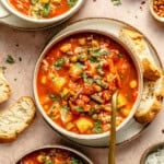 bowl of easy vegetable soup on a counter with a spoon dipped into it and slices of bread laid around it.