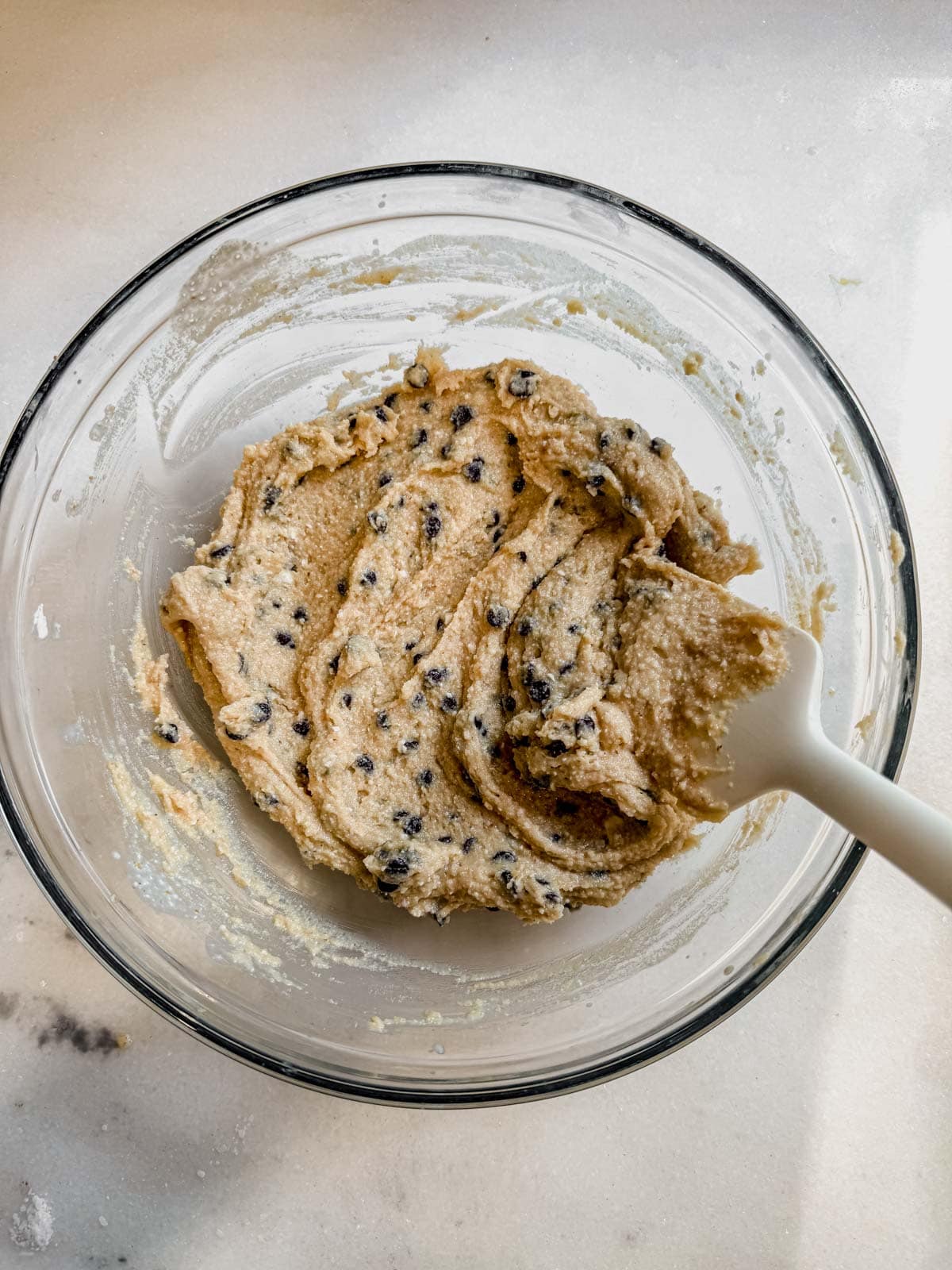 stirring mini chocolate chips into high protein cottage cheese cookie dough in a a glass bowl.