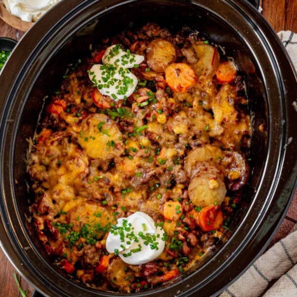 cowboy casserole in a crock pot topped with sour cream and chives.