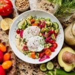 a mediterranean breakfast bowl with cucumber salad, hummus, and 2 poached eggs.