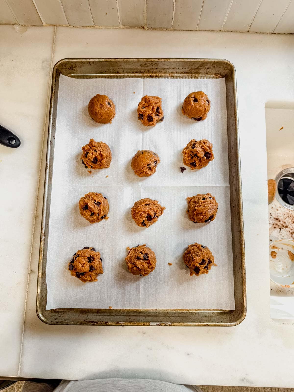 chocolate chip protein cookie dough balls on a parchment lined baking sheet.