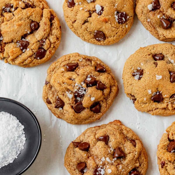 fresh baked protein cookies on a piece of parchment paper with a bowl of flaky salt.