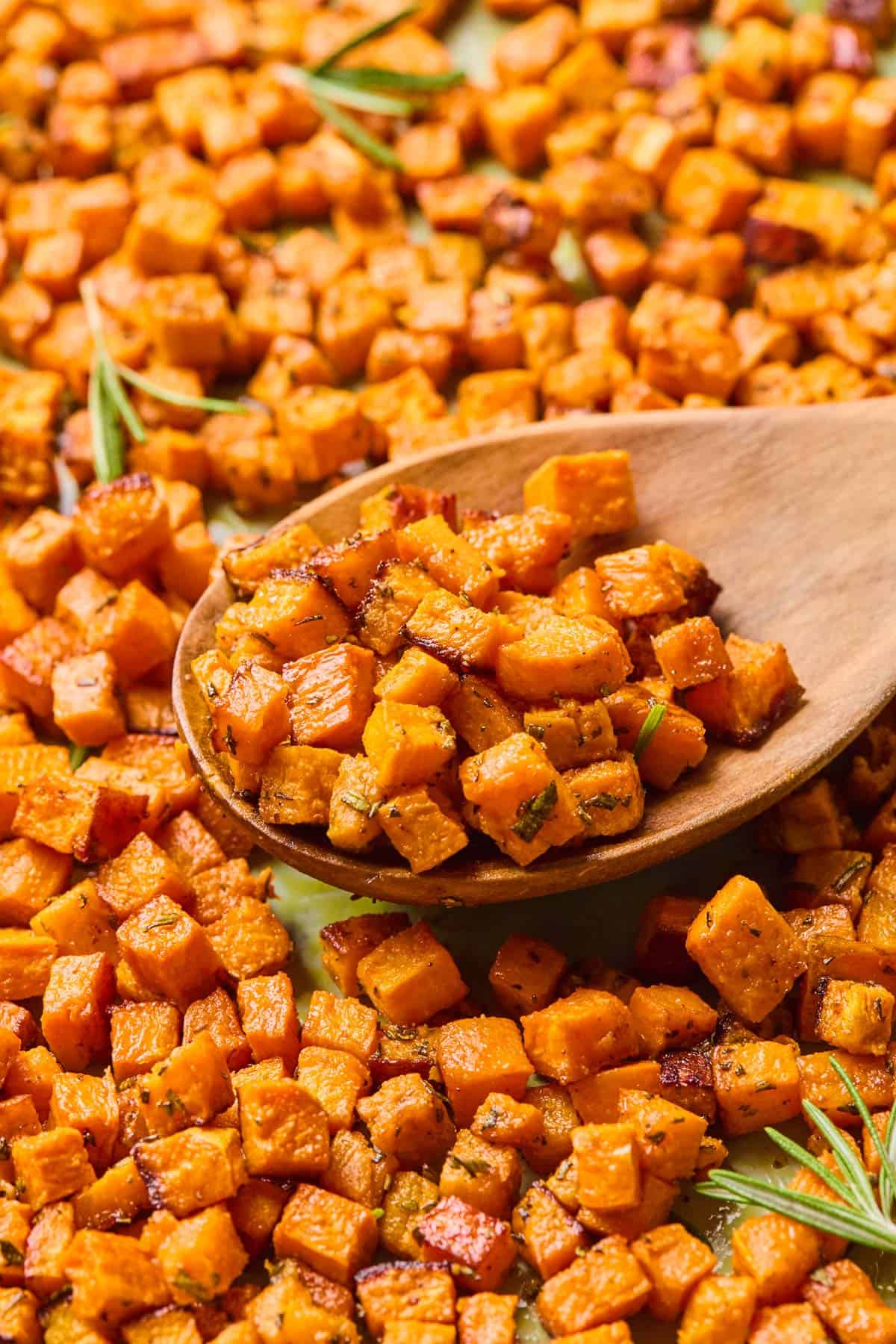 wooden spoon scooping up rosemary roasted sweet potatoes garnished with extra rosemary.
