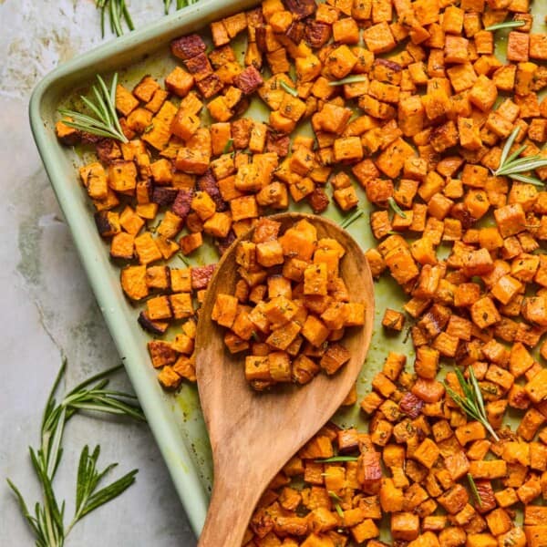 wooden spoon scooping up rosemary roasted sweet potatoes off of a baking sheet