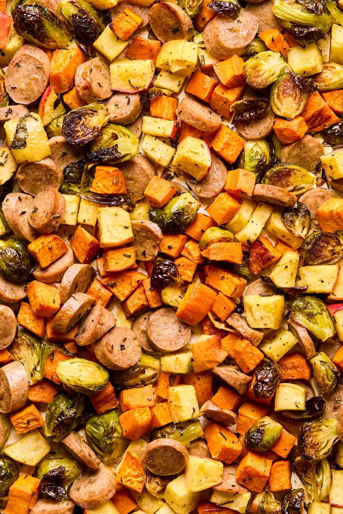 chicken sausage added to sheet pan of roasted veggies with maple dijon dressing poured overtop.